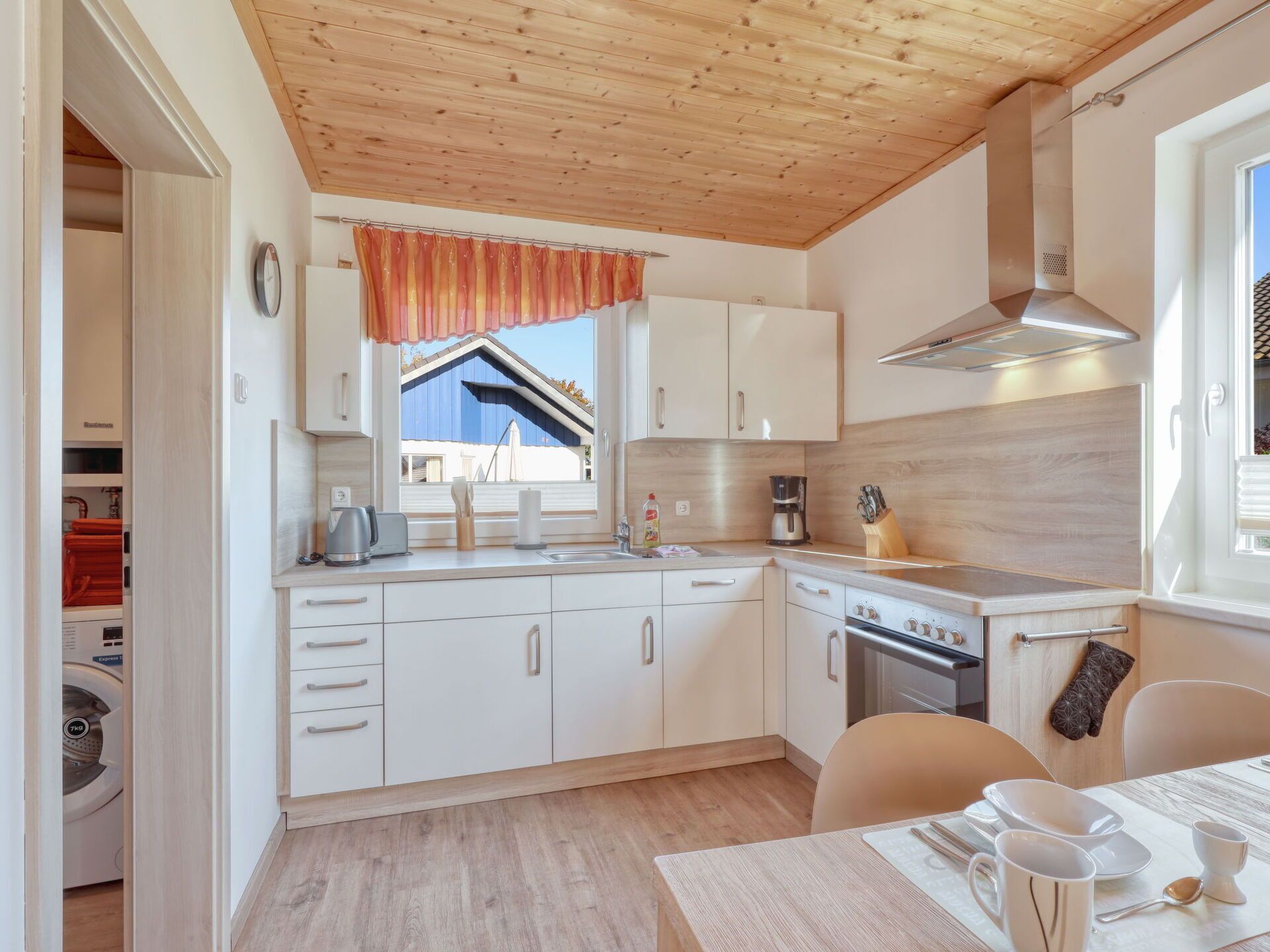 A modern kitchen with white cabinets, a wooden ceiling, and a window with a view of a blue building.