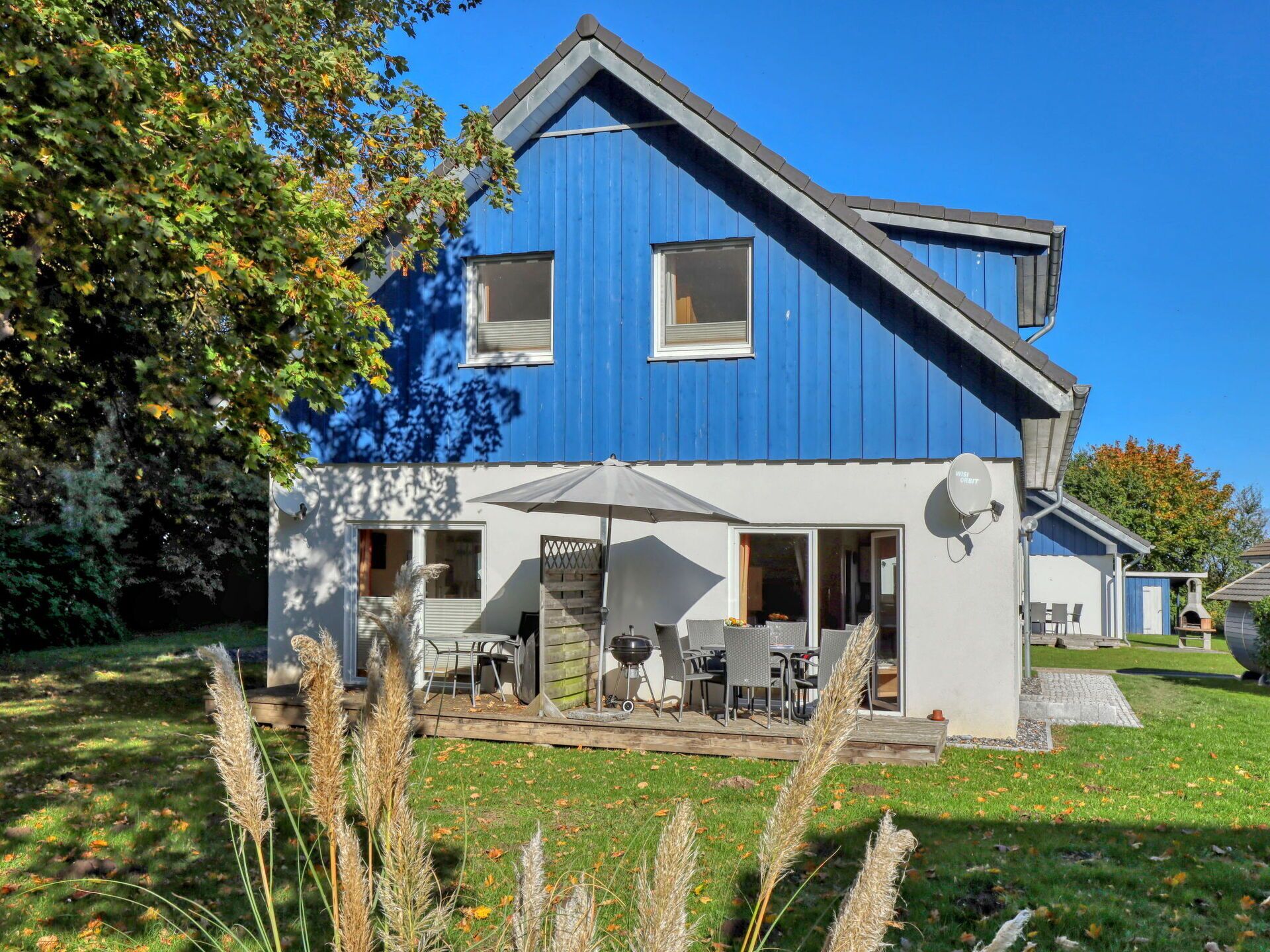 Een blauw gebouw met een schuin dak, een terras en een barbecue.