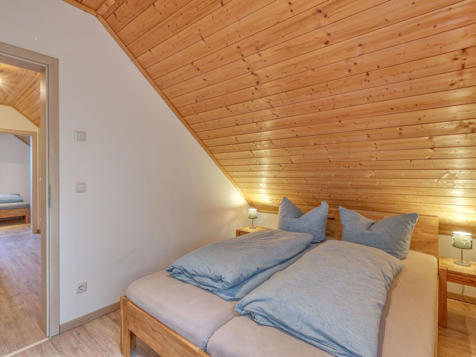A bedroom with a sloped ceiling, wooden headboard, and two bedside tables with lamps.