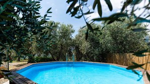 A rectangular swimming pool with a wooden deck surrounding it, set in a backyard with dense greenery and a wooden fence in the background. - Beautiful apartment for 6 people with A/C, WIFI, pool, patio, pets allowed and panoramic view (Civezza)