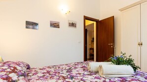 A bedroom with a floral bedspread, a wooden wardrobe, and a small plant on the bedside table. - Beautiful apartment for 6 people with A/C, WIFI, pool, patio, pets allowed and panoramic view (Civezza)