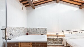 Une salle de bain avec une grande baignoire, un meuble en bois, un lit et un mur en pierre.