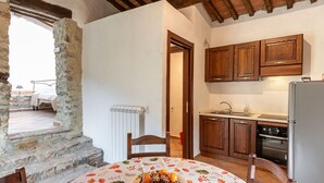 Une cuisine rustique avec des meubles de rangement en bois, un réfrigérateur et une table à manger agrémentée d’un panier de fruits.