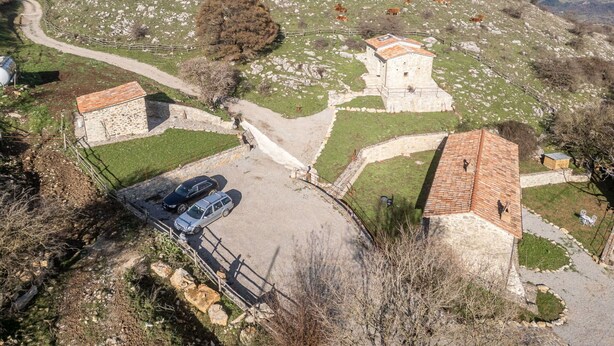 Un paysage rural avec des bâtiments en pierre, un chemin pavé et du bétail en pâturage.