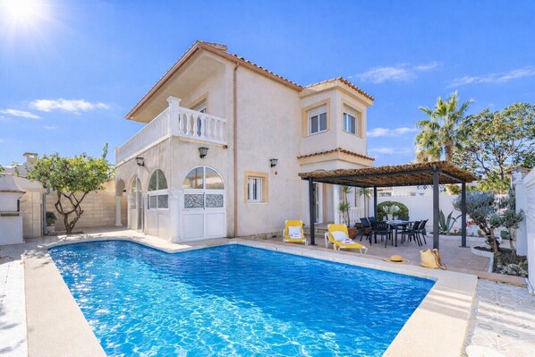 Ein zweistöckiges Haus mit Swimmingpool, Außenbereich und einer Pergola.