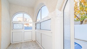 A narrow hallway with patterned floor tiles, a window with a view of buildings, and a door with frosted glass panels. - 0007-REQUESENS House with private pool and wifi (Empuriabrava)
