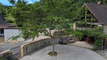 Un patio de grava con un árbol, un muro de piedra y un edificio con techo de tejas.