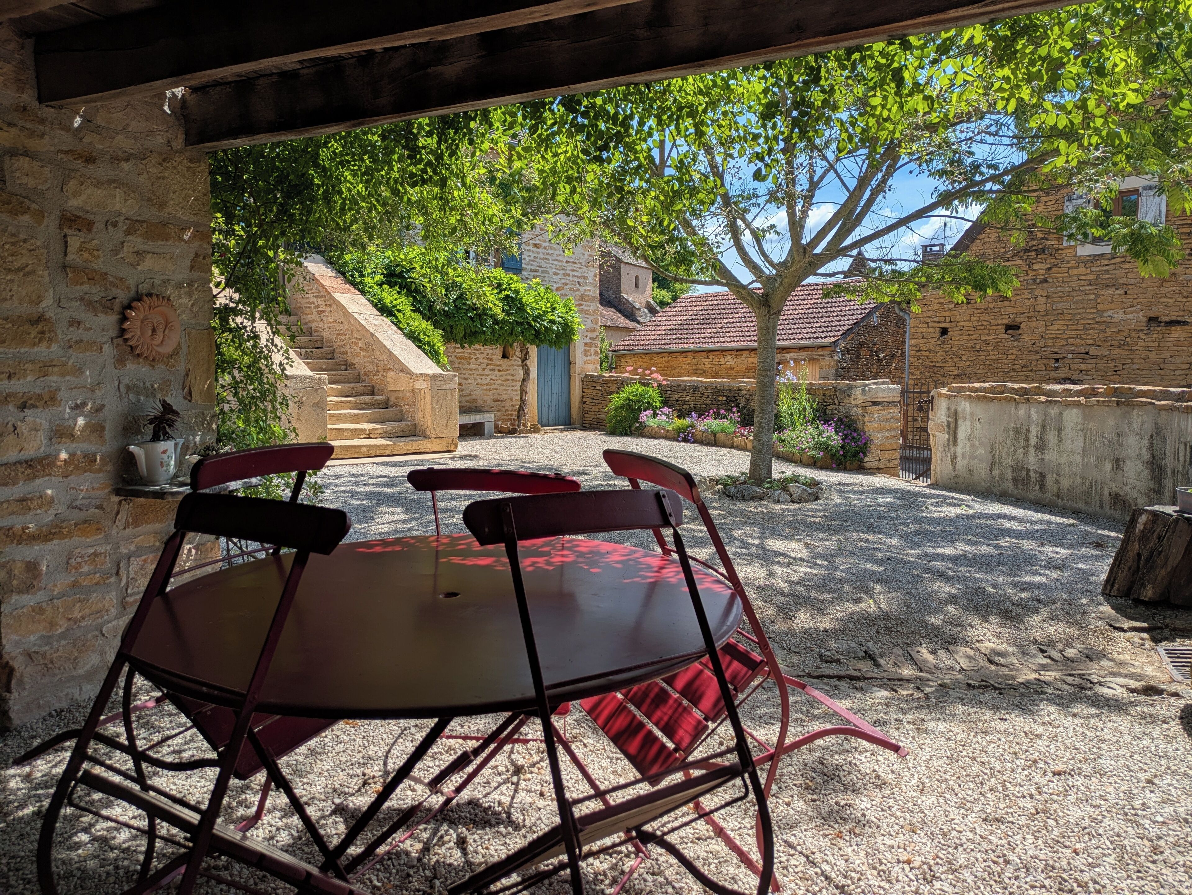 An outdoor patio with a round table and four chairs, surrounded by stone walls and a staircase leading to a building.
