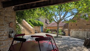 An outdoor patio with a round table and four chairs, surrounded by stone walls and a staircase leading to a building. - Chez Max et Juliette - Traditional Stone house in historic Burgundy village (Burnand)