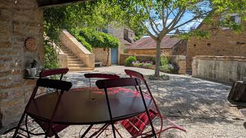 An outdoor patio with a round table and four chairs, surrounded by stone walls and a staircase leading to a building.