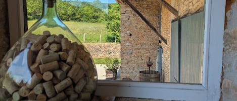 A bottle filled with corks on a windowsill, with a view of a stone building and greenery outside.