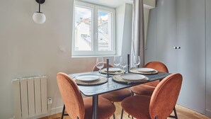 A dining area with a table set for four, a radiator, a window with curtains, and a grey wardrobe. - Charming Flat 1 Bedroom Le Marais Beaubourg (Paris)
