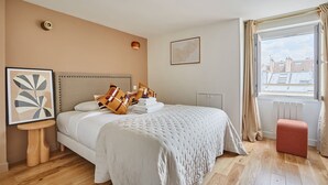 A hotel room with a large bed, a small table, a radiator, and a window with curtains. - Charming Flat 1 Bedroom Le Marais Beaubourg (Paris)
