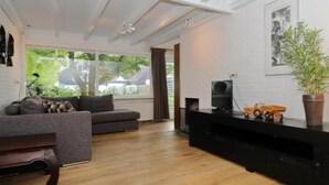 Una sala de estar moderna con un sofá gris, piso de madera, un mueble de entretenimiento negro y un ventanal con vistas al exterior.