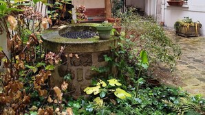 A courtyard with a stone fountain, potted plants, and a staircase leading to an upper level.