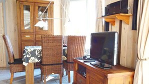 Ein Zimmer mit Esstisch, Korbstühlen, einem Fernseher auf einer Holzkommode und einer Kommode mit Schubladen.