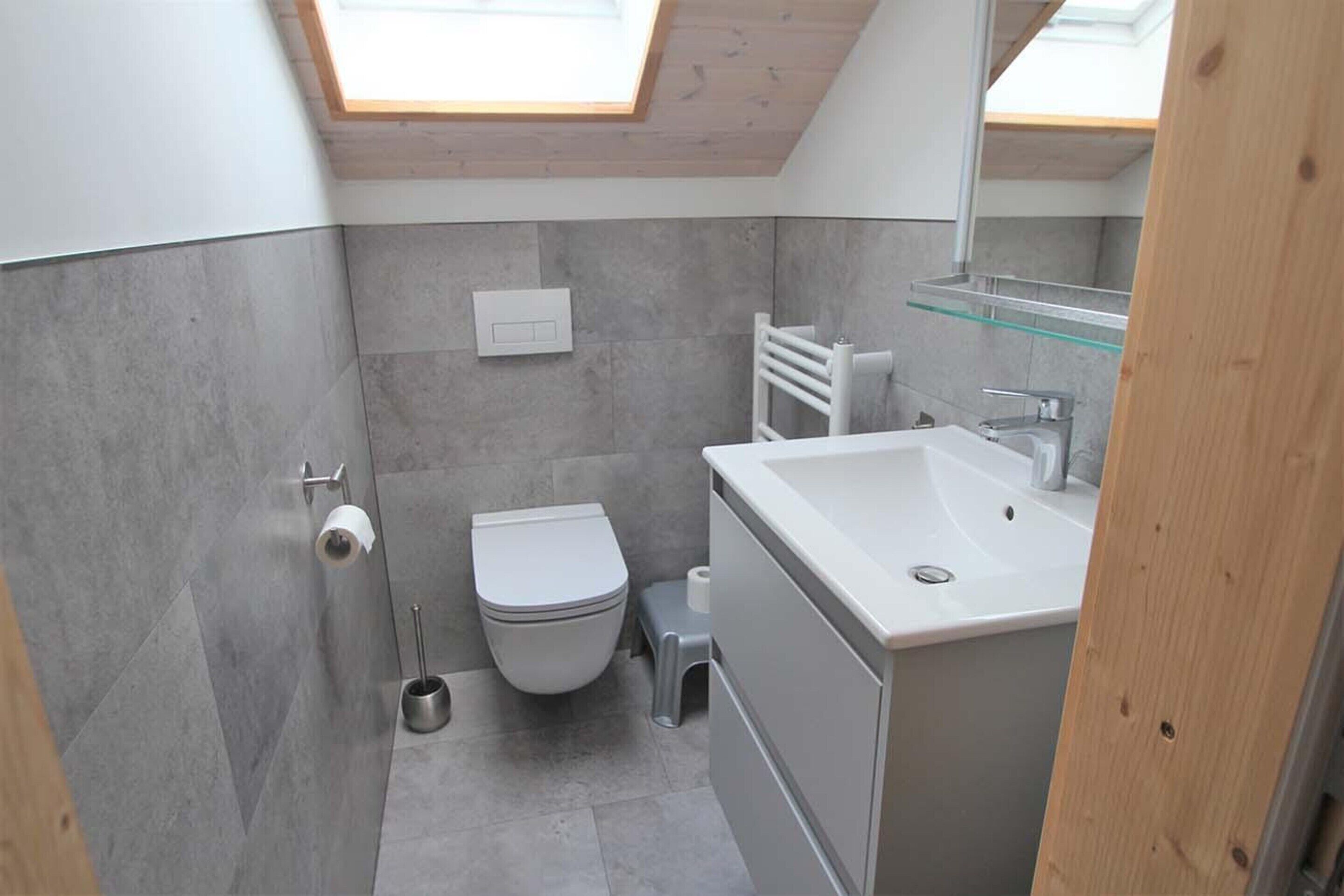 Une salle de bain moderne avec un puits de lumière, des toilettes, un lavabo et un miroir.