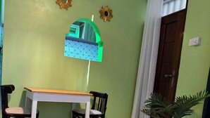 Una habitación con una mesa de madera, dos sillas, una pared verde, un reloj y una ventana con un diseño geométrico.
