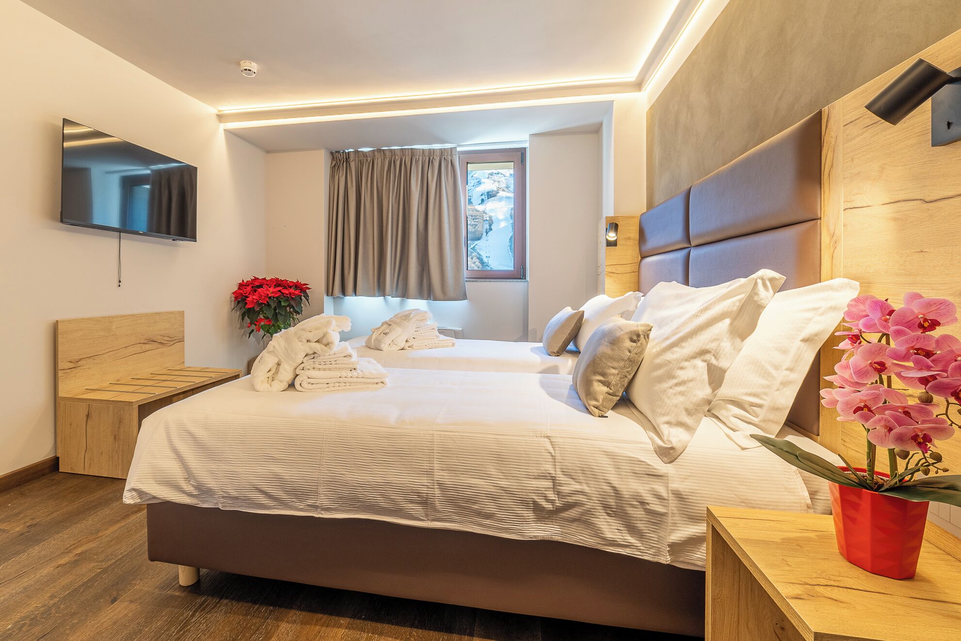 A modern hotel room with a large bed, a flat-screen TV, a wooden headboard, and a window with curtains.