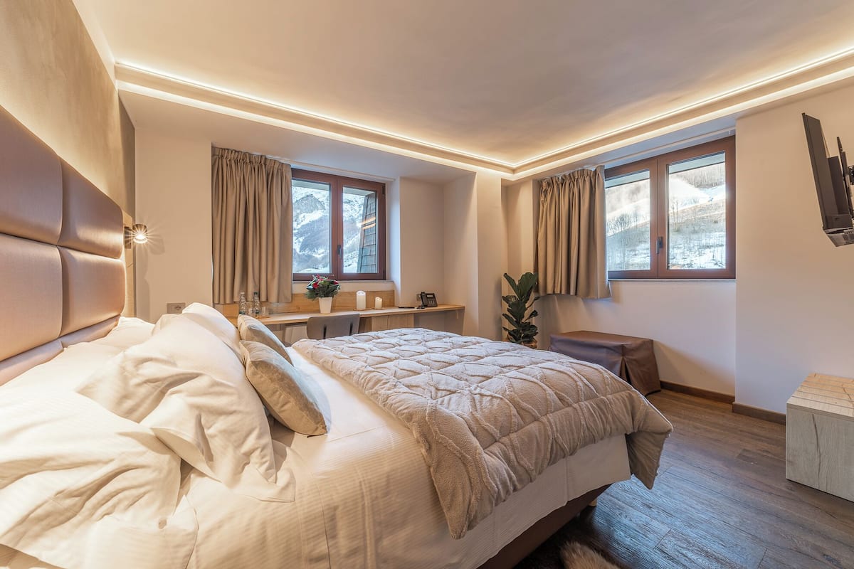 A modern bedroom with a large bed, bedside tables, a desk, and a view of a snowy landscape through the windows.