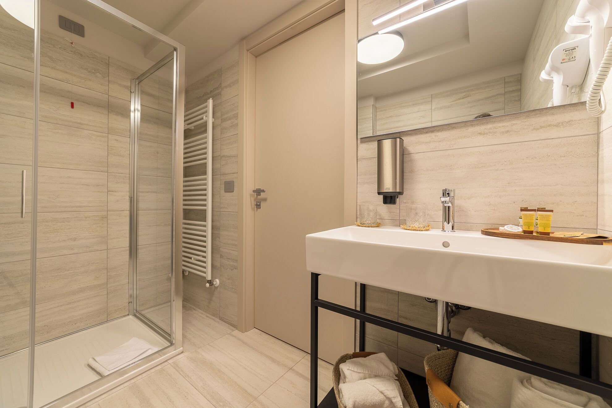 A modern bathroom with a glass shower enclosure, a white sink with a mirror above it, and a towel rack.