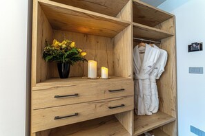 A wooden wardrobe with two drawers, a vase with yellow flowers, two lit candles, and a white robe hanging on a rack.