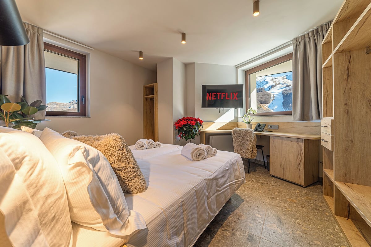 A hotel room with a bed, a desk, a TV, and a view of the mountains.