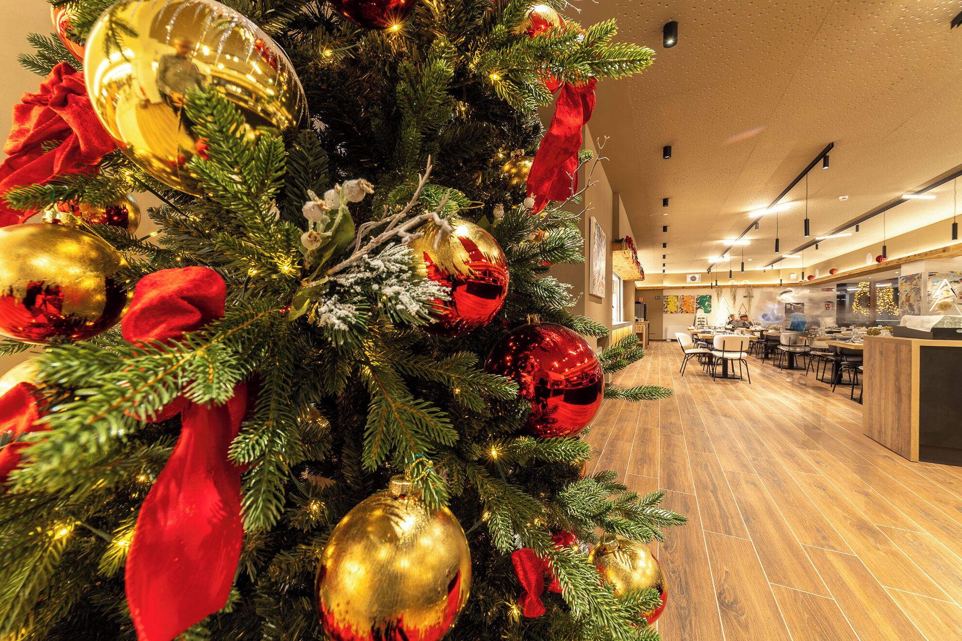 A Christmas tree with ornaments and a red bow, a wooden floor, and a dining area with tables and chairs.