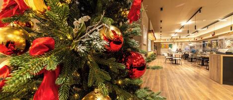 A Christmas tree with ornaments and a red bow, a wooden floor, and a dining area with tables and chairs.