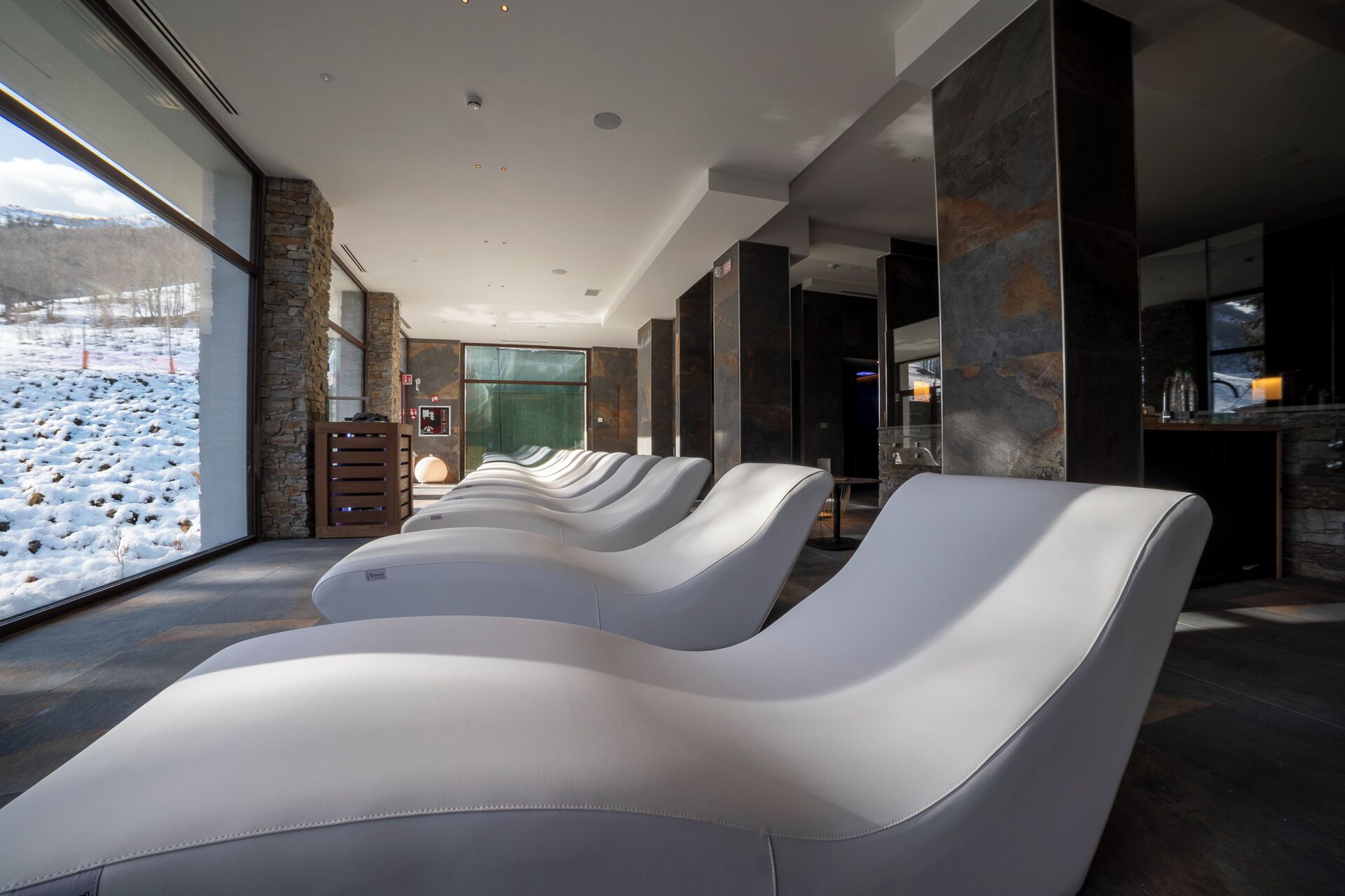Un área de spa con sillones reclinables, una pared de piedra y vistas a un paisaje nevado.