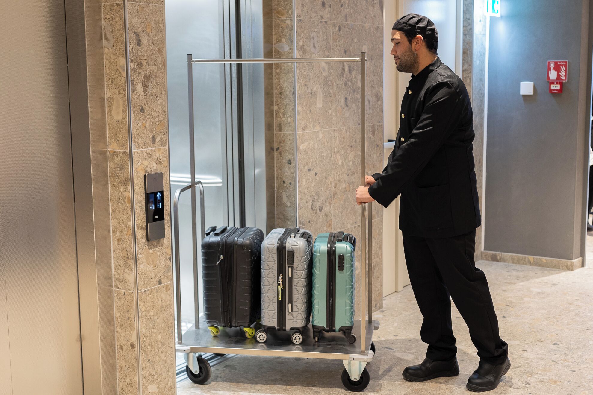 A person pushing a luggage cart with multiple suitcases in an elevator.