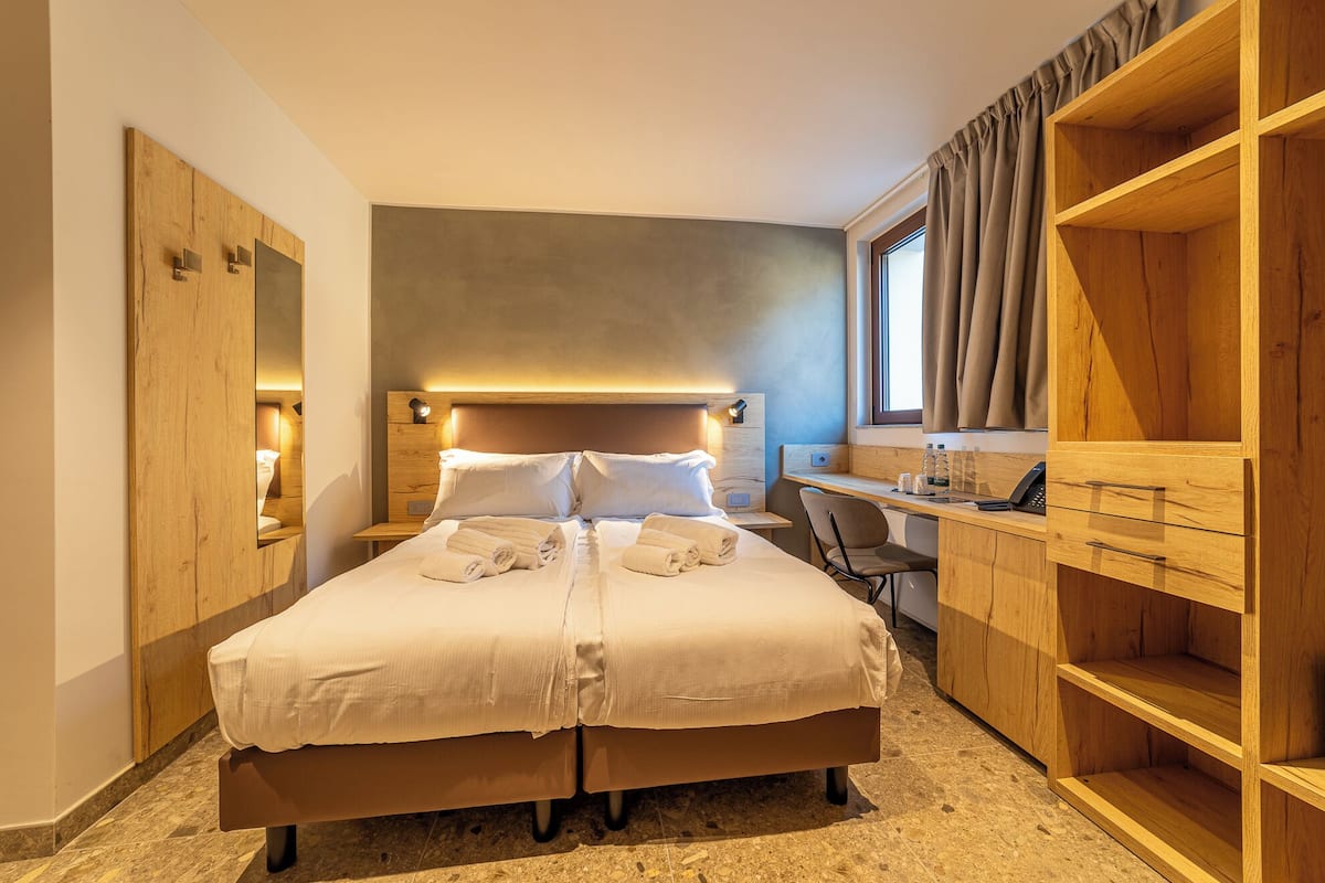 A hotel room with a large bed, a desk, a chair, and a wardrobe.