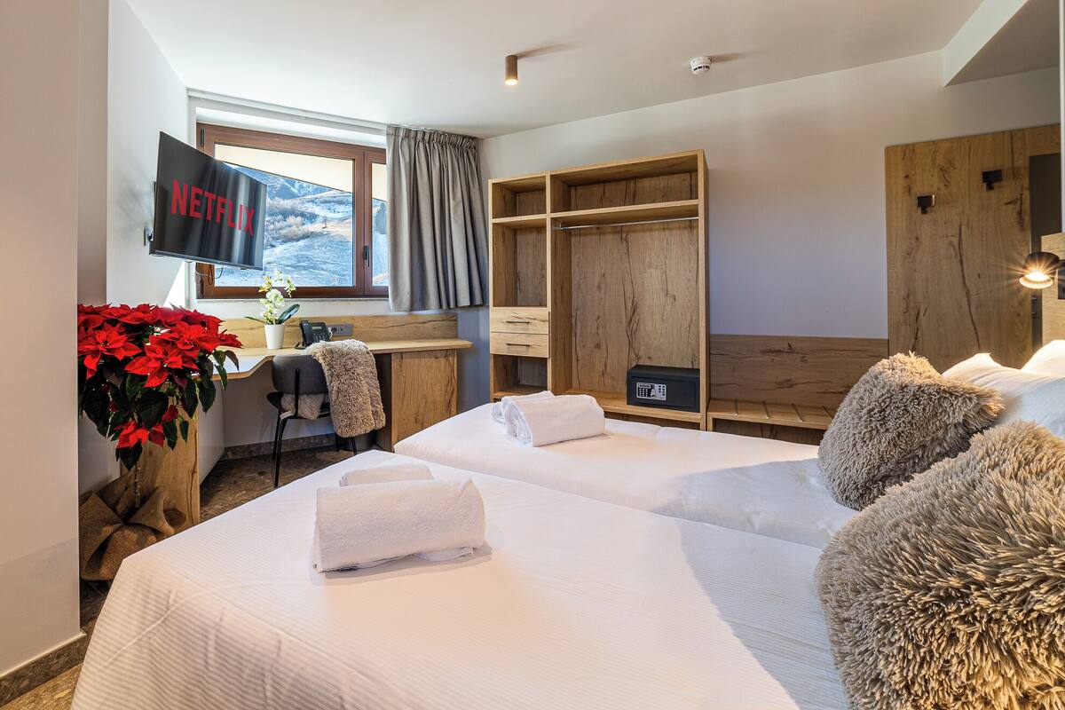 A hotel room with two beds, a desk with a computer, a TV, and a large window.