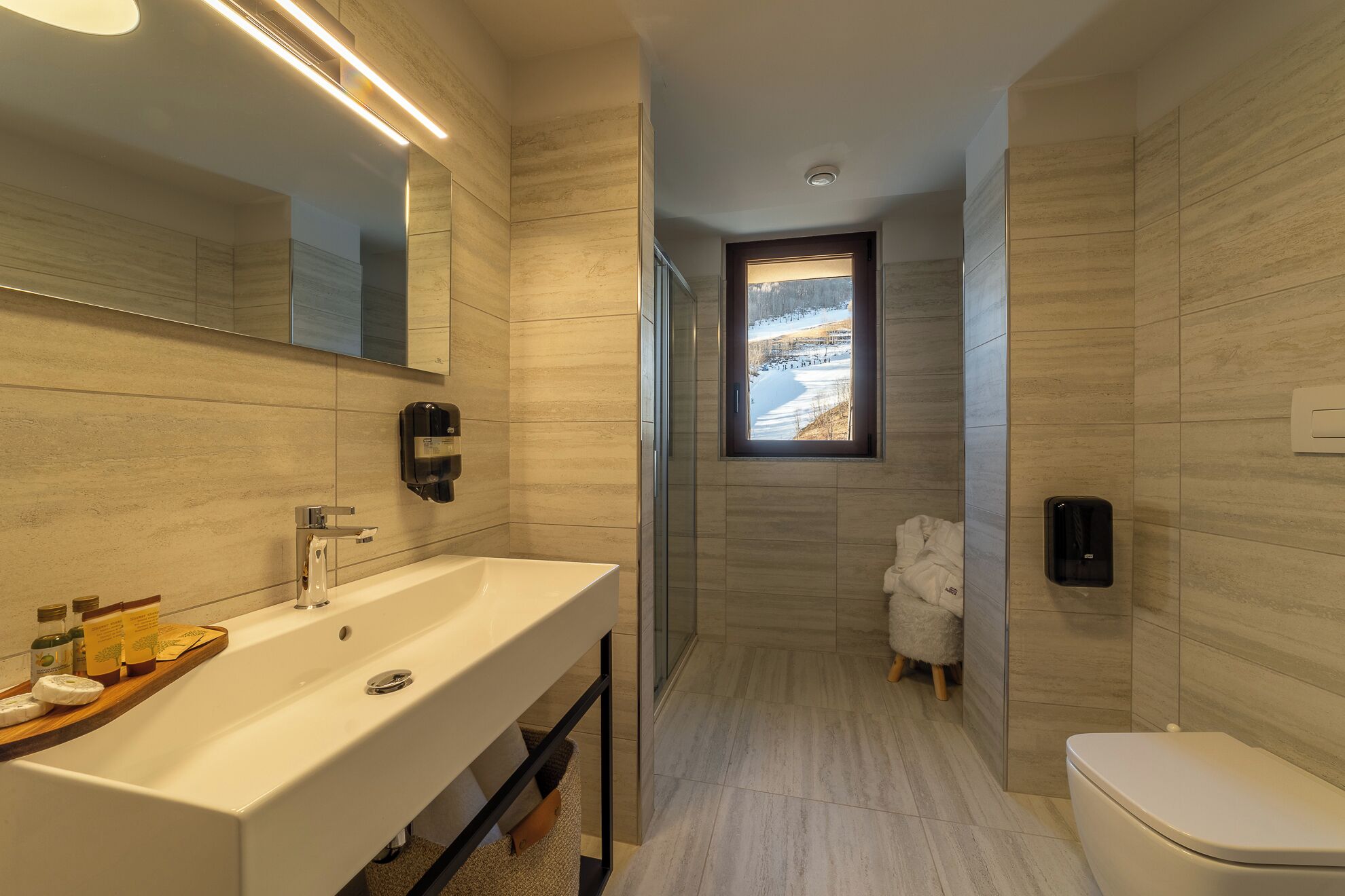 A modern bathroom with a large sink, a toilet, and a window with a view of a snowy landscape.
