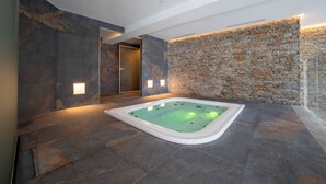 A modern spa room with a stone wall, a stone floor, and a hot tub. - Riserva Bianca Limone Hotel&SPA (Limone Piemonte)