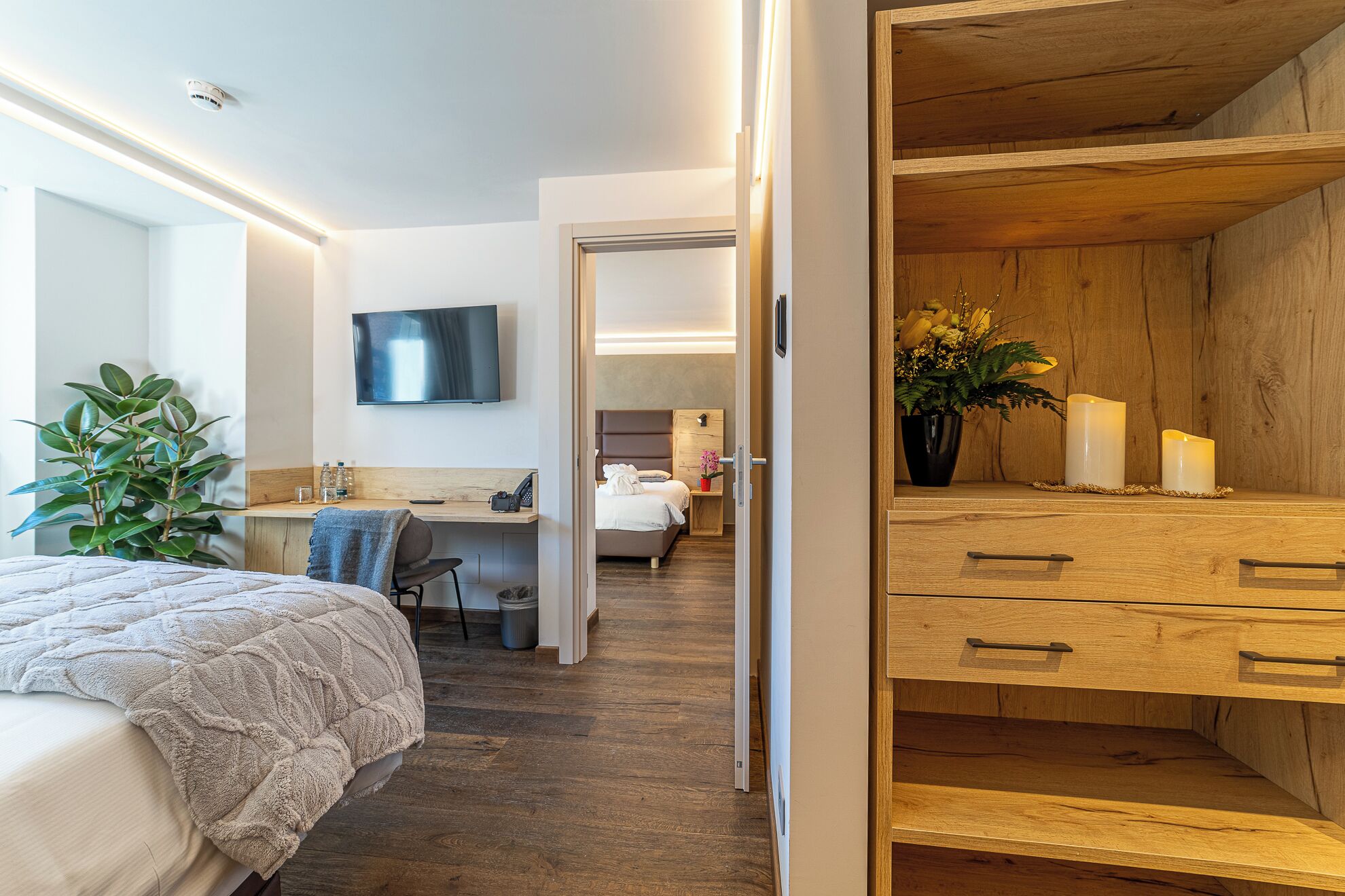Habitación de hotel con una cama, un escritorio con silla, un televisor y un aparador de madera con cajones.
