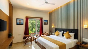 A hotel room with a large bed, a desk, a chair, a television, and a window with curtains. - Weekender Resort (Udaipur)