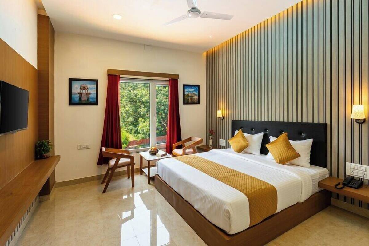 A hotel room with a large bed, a desk, a chair, a television, and a window with curtains.