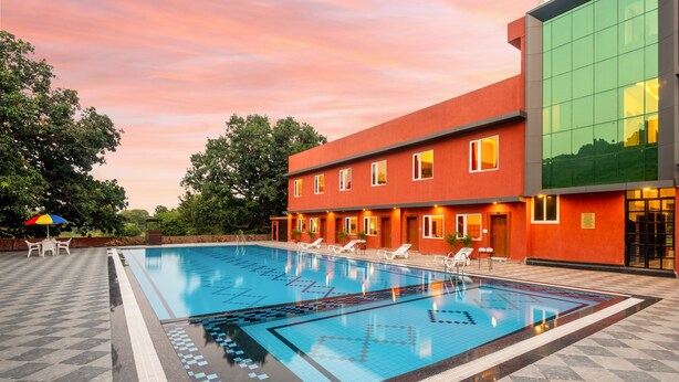 A swimming pool with a tiled deck, lounge chairs, and a modern building with large windows. - Weekender Resort (Udaipur)