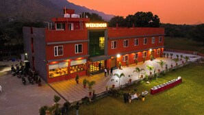 A hotel named "Weekend" with a red facade, multiple windows, and a paved courtyard with potted plants. - Weekender Resort (Udaipur)