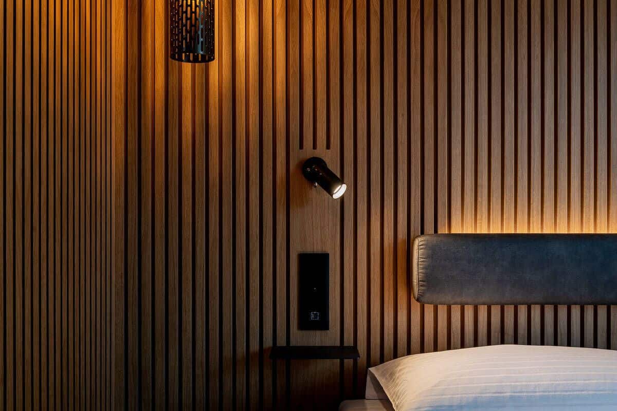 Une chambre d’hôtel avec un mur en lambris de bois, une table de chevet avec une lampe et un lit doté d’une tête de lit.