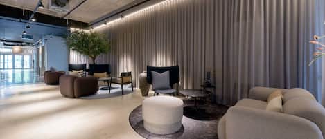 A modern lounge area with a round seating arrangement, a large potted plant, and a curtain wall.
