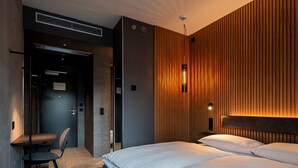A modern hotel room with a large bed, a desk with a chair, and a wooden accent wall.
