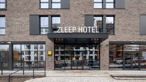 A Zleep Hotel with a modern brick facade, large glass entrance, and a visible car parking area.