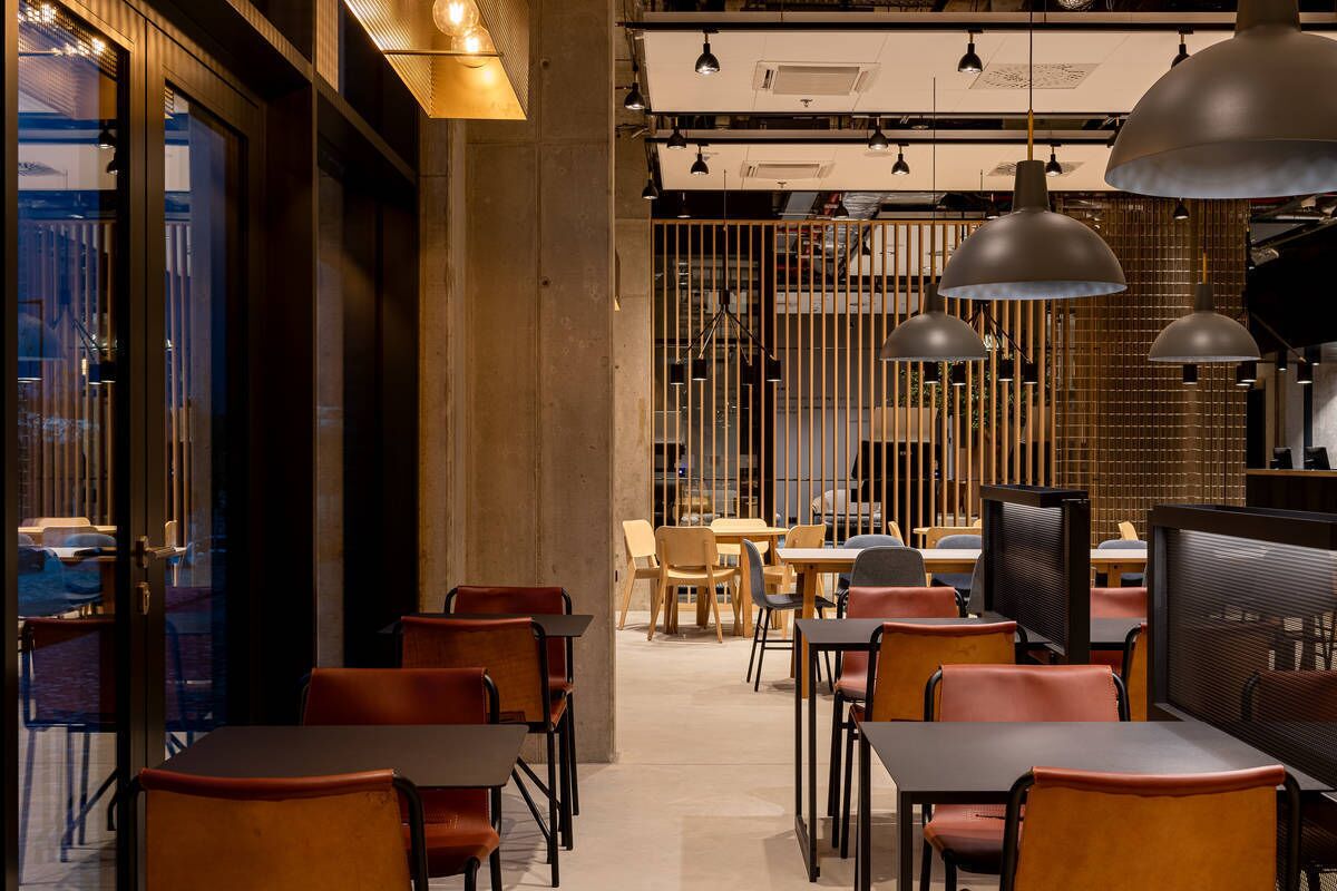 A modern restaurant interior with wooden furniture, pendant lighting, and a view through a glass door.