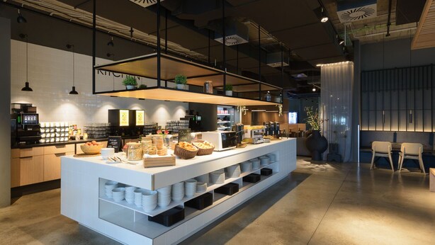 A modern cafe with a central serving counter, seating area, and a visible coffee machine.
