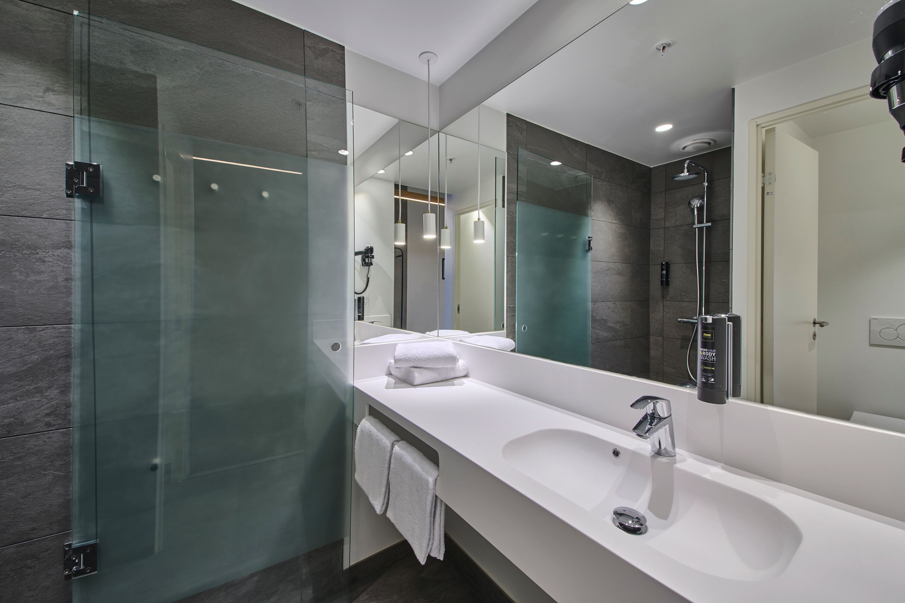 Un baño moderno con un espejo grande, un lavamanos blanco y una cabina de ducha de vidrio.