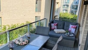 A balcony with a table and wicker chairs, a sofa with cushions, and a view of residential buildings.