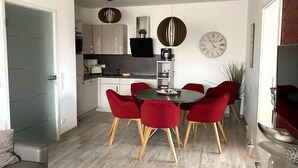 A modern kitchen with white cabinets, a black countertop, and a dining area with a round table and red chairs.
