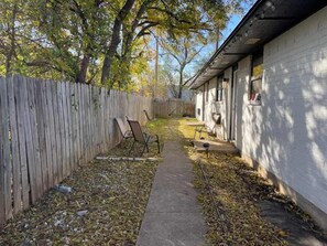 Un patio trasero con cerca de madera, un sendero de concreto y un edificio con ventana.